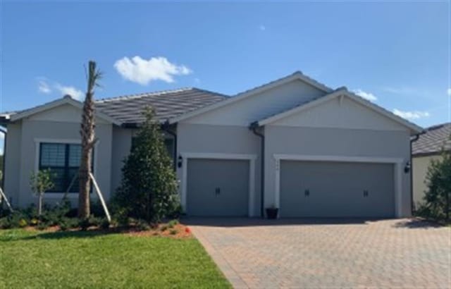 single story home featuring decorative driveway, a front yard, an attached garage, and stucco siding