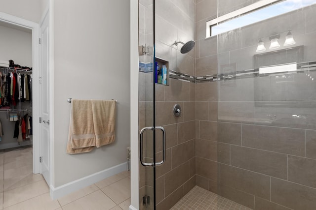 full bathroom featuring a stall shower, baseboards, tile patterned flooring, and a walk in closet
