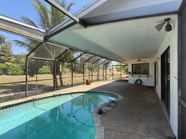 pool featuring glass enclosure, a patio, and ceiling fan