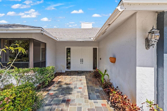 entrance to property with roof with shingles, stucco siding, and a chimney