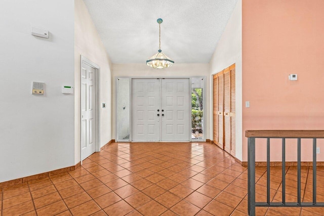tiled entryway with a notable chandelier, baseboards, a textured ceiling, and lofted ceiling