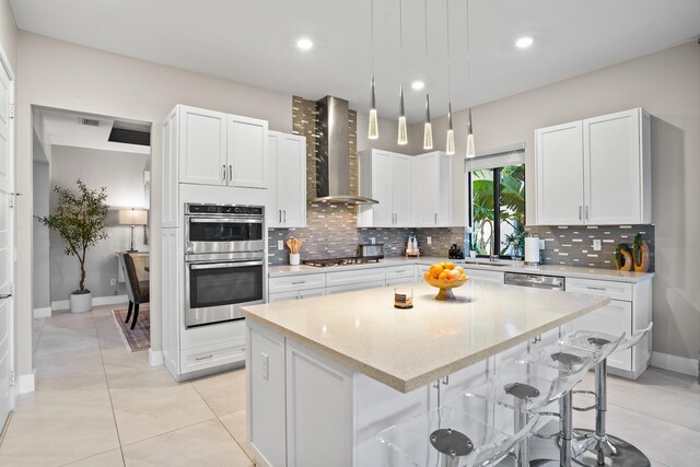kitchen featuring wall chimney range hood, a kitchen island, tasteful backsplash, white cabinets, and stainless steel appliances