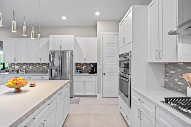 kitchen featuring decorative backsplash, wall chimney range hood, white cabinets, appliances with stainless steel finishes, and light tile patterned floors