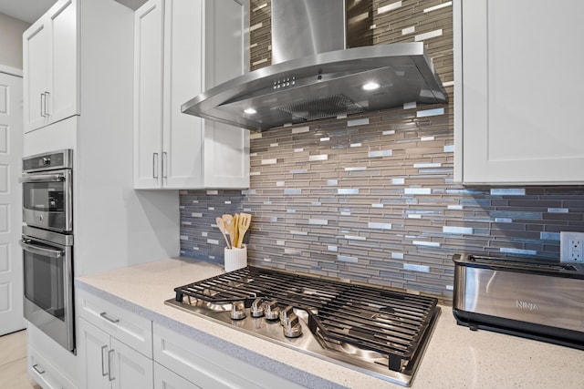 kitchen featuring white cabinetry, appliances with stainless steel finishes, wall chimney exhaust hood, and tasteful backsplash