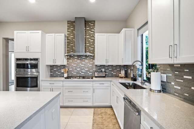 kitchen featuring wall chimney exhaust hood, white cabinets, a sink, appliances with stainless steel finishes, and backsplash