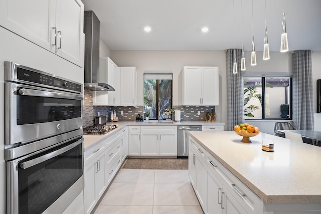 kitchen with decorative backsplash, wall chimney range hood, white cabinets, a sink, and appliances with stainless steel finishes