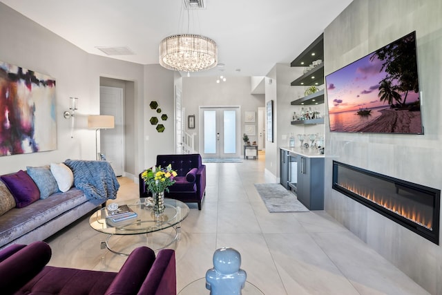 living area with visible vents, a glass covered fireplace, light tile patterned flooring, baseboards, and a notable chandelier