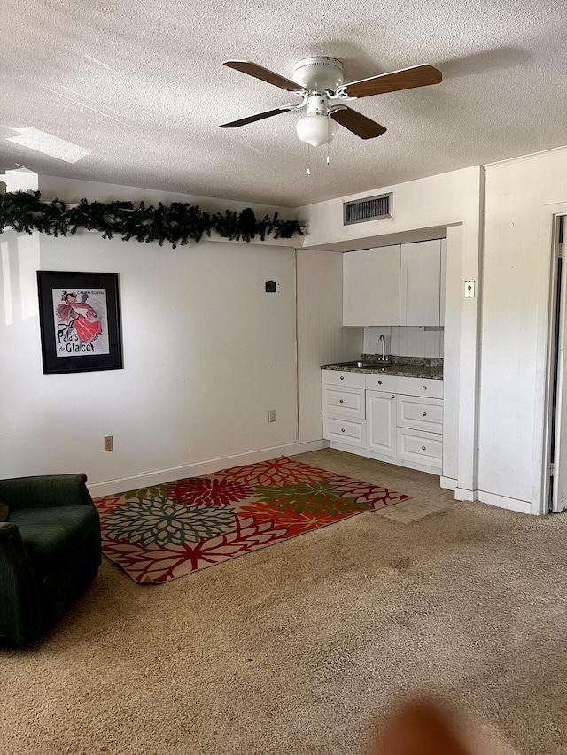 carpeted living room with visible vents, baseboards, a textured ceiling, a ceiling fan, and a sink