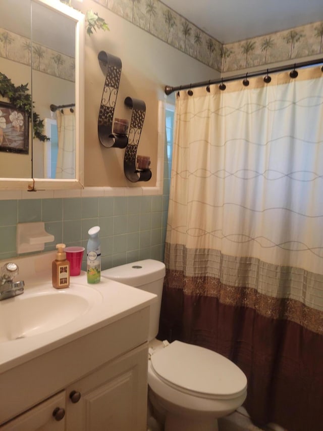 bathroom with curtained shower, toilet, vanity, wainscoting, and tile walls