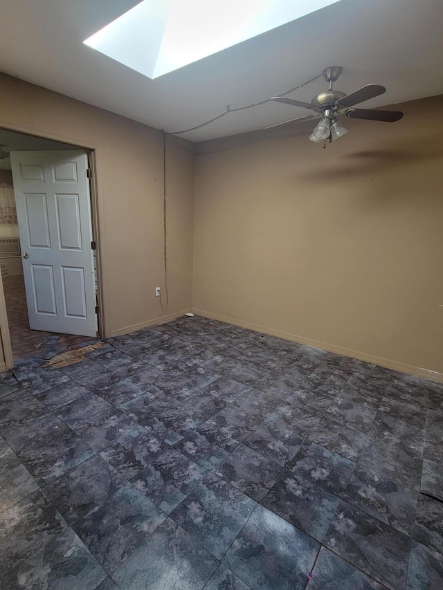 empty room featuring a skylight, a ceiling fan, and baseboards