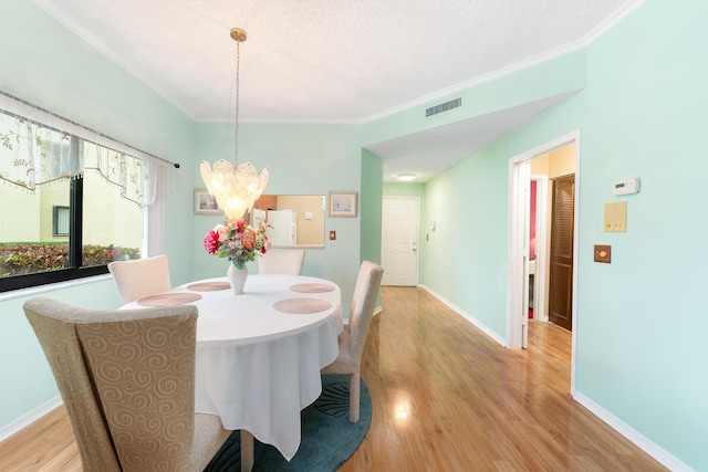 dining room with visible vents, crown molding, light wood-type flooring, and an inviting chandelier