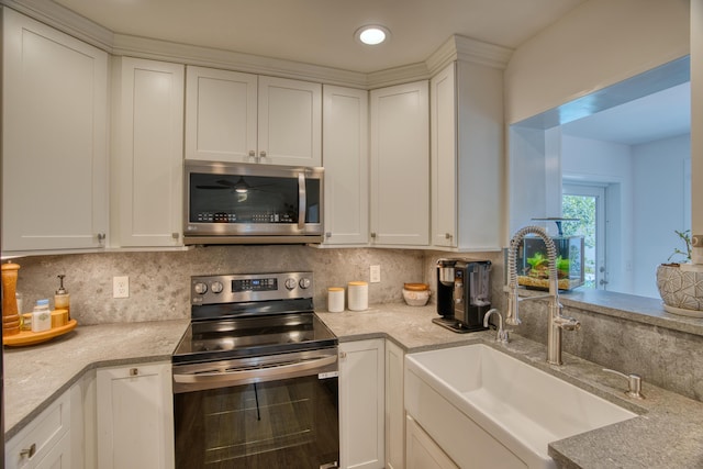 kitchen with backsplash, appliances with stainless steel finishes, white cabinetry, and a sink