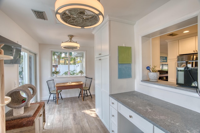 kitchen featuring visible vents, white cabinetry, dark stone counters, light wood finished floors, and baseboards