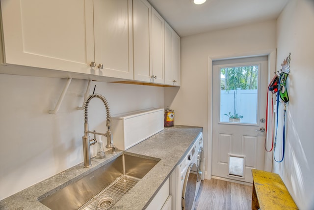 clothes washing area with a sink, cabinet space, wood finished floors, and washer and clothes dryer