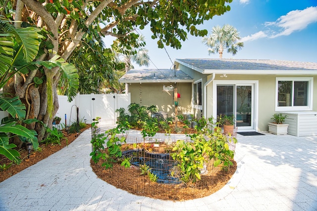 view of front of house featuring a shingled roof, fence, stucco siding, a patio area, and a gate