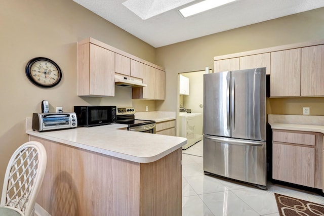 kitchen with light brown cabinets, under cabinet range hood, light countertops, appliances with stainless steel finishes, and washer and dryer