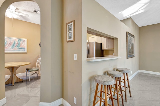 kitchen with a kitchen bar, baseboards, freestanding refrigerator, and ceiling fan