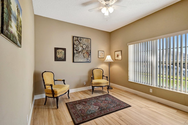 living area with a textured ceiling, baseboards, ceiling fan, and wood finished floors