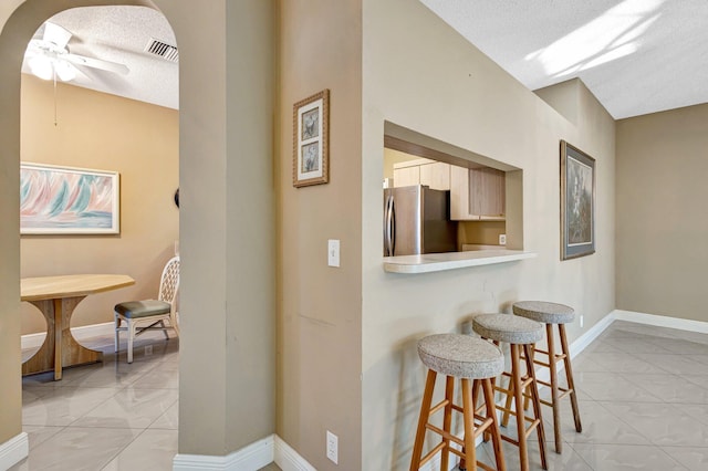 7848 Mansfield Hollow Rd, Delray Beach, FL 33446 - kitchen featuring freestanding refrigerator, a breakfast bar area, ceiling fan, light countertops, and a textured ceiling