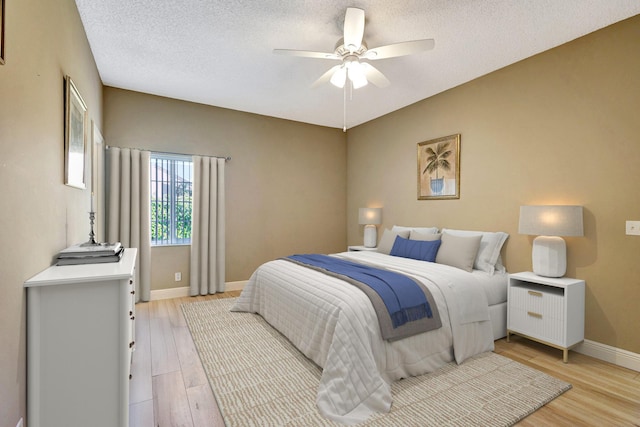 bedroom with light wood-type flooring, baseboards, a textured ceiling, and ceiling fan