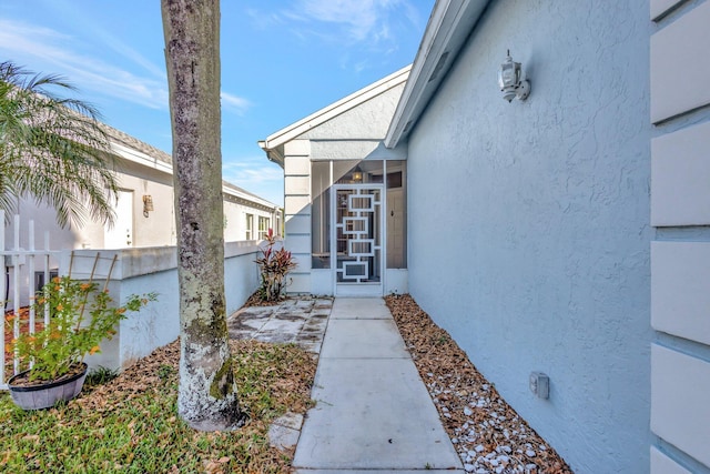 entrance to property featuring stucco siding and fence