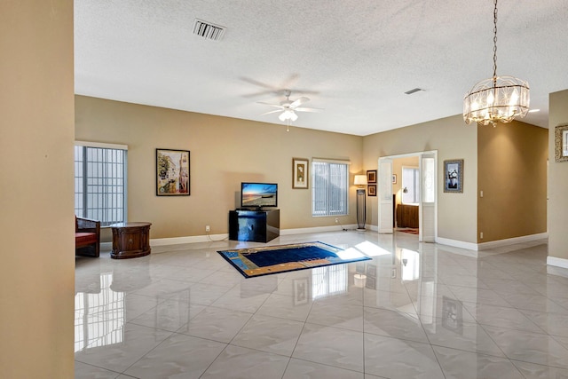 unfurnished living room with visible vents, ceiling fan with notable chandelier, a textured ceiling, and baseboards