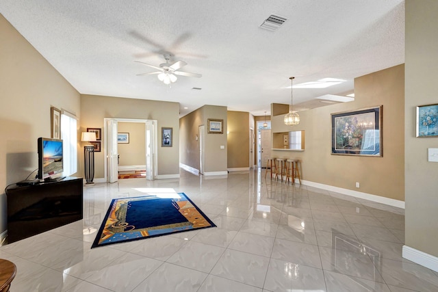 interior space with visible vents, ceiling fan with notable chandelier, a textured ceiling, and baseboards