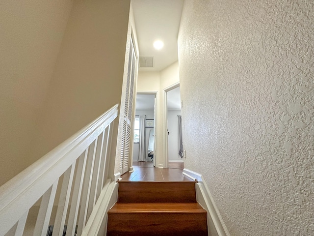 staircase with visible vents, baseboards, tile patterned flooring, and a textured wall