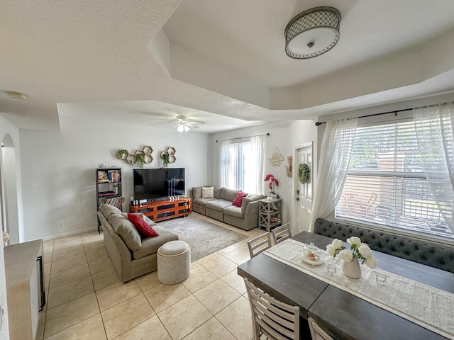 living room with light tile patterned floors, arched walkways, a textured ceiling, and ceiling fan