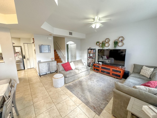 living area featuring light tile patterned floors, visible vents, arched walkways, ceiling fan, and stairs