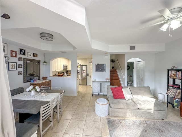 living area featuring visible vents, stairway, a tray ceiling, light tile patterned floors, and arched walkways