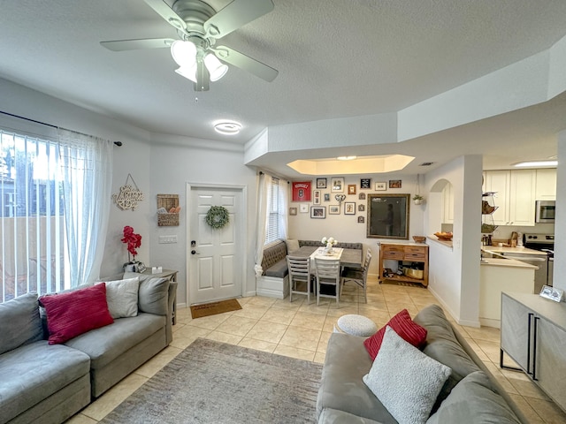 living area featuring light tile patterned flooring, arched walkways, a textured ceiling, and baseboards