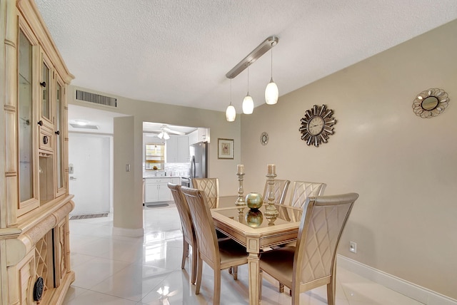 dining space with visible vents, a textured ceiling, light tile patterned flooring, baseboards, and ceiling fan