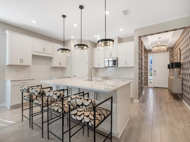 kitchen featuring stainless steel microwave, visible vents, a center island with sink, white cabinets, and a sink