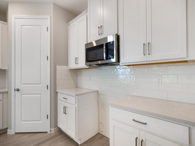 kitchen with wood finish floors, decorative backsplash, light countertops, white cabinetry, and stainless steel microwave