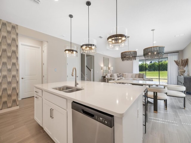 kitchen featuring a kitchen island with sink, a sink, light countertops, dishwasher, and open floor plan