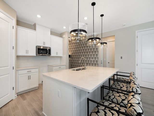 kitchen featuring a center island with sink, a sink, stainless steel microwave, tasteful backsplash, and white cabinets