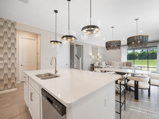 kitchen with open floor plan, dishwasher, light countertops, white cabinetry, and a sink