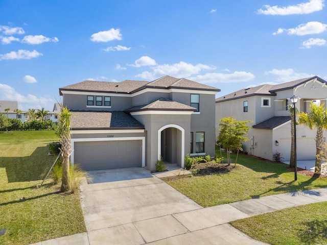 view of front facade featuring stucco siding, driveway, a front yard, and a shingled roof