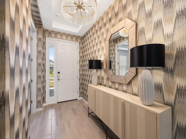 foyer with wallpapered walls, a tray ceiling, baseboards, and light wood-type flooring