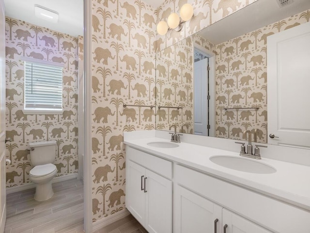 full bath with double vanity, toilet, wallpapered walls, and a sink