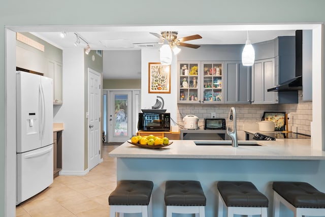 kitchen with a sink, decorative backsplash, white fridge with ice dispenser, and a peninsula