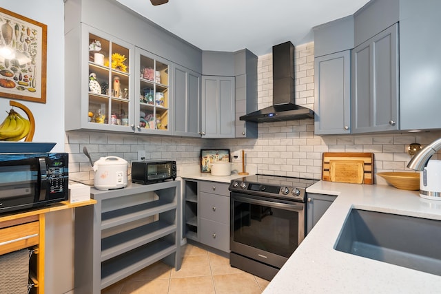 kitchen with black microwave, wall chimney range hood, stainless steel electric range oven, light countertops, and gray cabinets