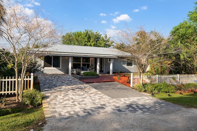 view of front of home with a fenced front yard, decorative driveway, covered porch, and metal roof