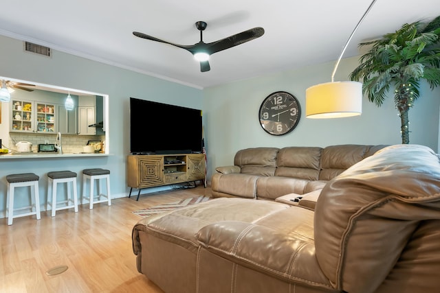 living area with visible vents, wood finished floors, a ceiling fan, and ornamental molding