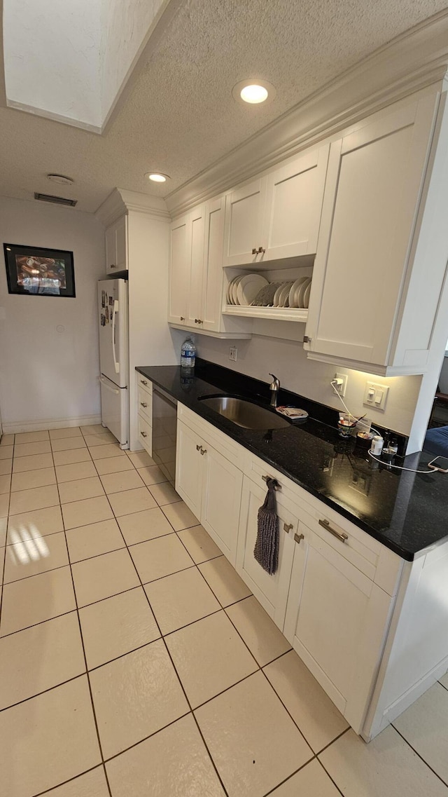 kitchen featuring light tile patterned floors, freestanding refrigerator, a sink, dishwasher, and dark countertops