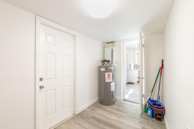 below grade area with light wood-style flooring, baseboards, and electric water heater