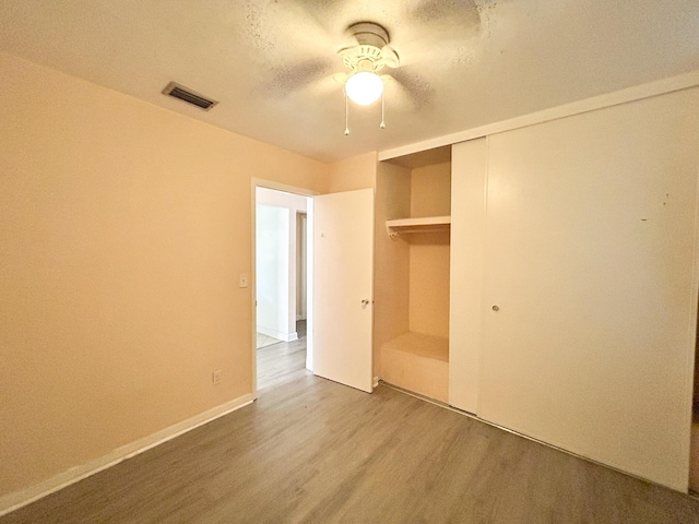 unfurnished bedroom with visible vents, wood finished floors, a closet, baseboards, and ceiling fan