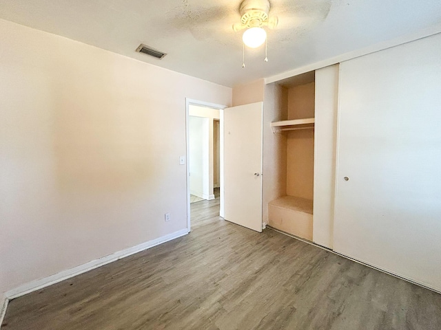 unfurnished bedroom with a ceiling fan, visible vents, wood finished floors, baseboards, and a closet