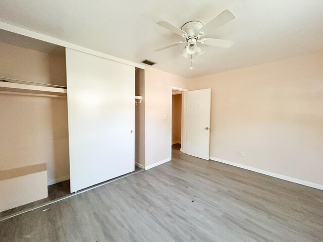 unfurnished bedroom with wood finished floors, visible vents, baseboards, ceiling fan, and a closet